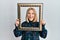 Young blonde woman holding empty frame smiling and laughing hard out loud because funny crazy joke