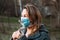 A young blonde woman inhales the smell of a flower through a medical mask