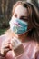 A young blonde woman inhales the smell of a flower through a medical mask