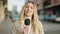 Young blonde woman journalist speaking using microphone at street