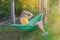 Young blonde woman lies in green tourist hammock on nature