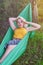 Young blonde woman lies in green tourist hammock on nature