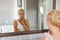 Young blonde woman loking at the mirror in bathroom