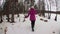 Young blonde woman in pink coat running in winter forest