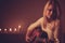 Young blonde woman playing guitar in candle light