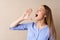 Young blonde woman screaming something loud, making announcement, against beige background