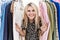 Young blonde woman searching clothes on clothing rack smiling with a happy and cool smile on face