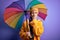 Young blonde woman with short hair wearing waterproff raincoat and colorful umbrella cover mouth with hand shocked with shame for