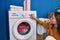 Young blonde woman sitting on floor turning washing machine on at laundry room