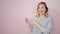 Young blonde woman smiling pointing to the side over isolated pink background