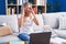 Young blonde woman studying using computer laptop at home with hand on head, headache because stress