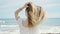 Young blonde woman tourist touching hair standing backwards at beach