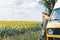 Young blonde woman travelling by campervan. Overlooking sunflower field on sunny summer day