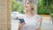 Young blonde woman using smartphone holding bottle of water at street