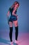 Young blonde woman in velour blue sport wear and black stockings seductively posing on camera in studio. Pink and blue