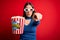 Young blonde woman wearing 3d glasses and eating pack of popcorn watching a movie on cinema pointing displeased and frustrated to