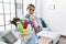 Young blonde woman wearing cleaner uniform holding cleaning products serious face thinking about question with hand on chin,