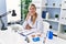 Young blonde woman wearing dentist uniform sitting on table at clinic