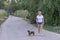 A young blonde woman in a white T-shirt and shorts walks in the park with a brown dachshund. Walking the dog outdoors in summer