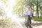 Young blonge woman walking her bicycle in the park and holding a cup of coffee