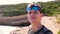 Young blue-eyed guy with two sunglasses makes a selfie against the backdrop of nature, the bay, the rocks with green