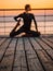 Young blurred woman doing yoga exercises on wooden sea embankment in the morning. Girl in black sports costume