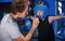 Young boxing coach is helping little boy in protective wear and with blood under nose on the ring between the rounds