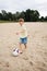 A young boy on the beach runs towards a soccer ball and wants to score a goal