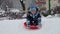 Young boy with a big smile as he slides down a snowy slope on his plastic sled, footage captured in slow motion.