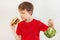 Young boy chooses between hamburger and fresh broccoli on white background