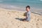 Young boy face. Kid playing with sand on the beach alone. Little boy near sea. Summer play