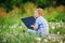 Young boy in field with dandelions with a laptop