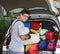 Young boy with glasses puts suitcases in the luggage of the car