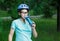 Young boy in helmet and green t shirt cyclist drinks water from bottle in the park. Smiling cute Boy on bicycle in the forest