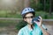 Young boy in helmet and green t shirt cyclist drinks water from bottle in the park. Smiling cute Boy on bicycle in the forest