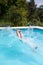 Young boy jumps into the clear blue water of the pool. Unrecognizable person