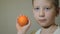 Young boy looking happy at camera and keep a mandarin. Slow motion.