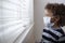 Young boy looking out the window wearing a protective facemark while seeking protection from COVID-19, or the novel coronavirus