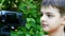 Young boy looks into video camera on background of green park.