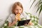 A young boy lounges on the bed, engrossed in his tablet, snacking on a pastry