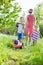 Young boy mowing grass with lawn mower, his mother and sister encouraging him