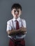 Young boy in school uniform feeling upset and angry looking unhappy and moody posing with folded arms on isolated background