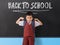 Young boy in school uniform infornt of black board with `back to school` written in white chalk