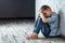 A young boy sits alone with a sad feeling at school near the wall. Offended child abandoned in the corridor and bent against a