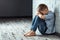 A young boy sits alone with a sad feeling at school near the wall. Offended child abandoned in the corridor and bent against a