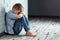 A young boy sits alone with a sad feeling at school near the wall. Offended child abandoned in the corridor and bent against a