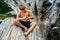 Young boy sitting on a fallen tree trunk, and focusing on to carving a wooden stick for the grill with a small knife