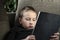 Young boy sitting on sofa in living room and watching cartoons on tablet. Portrait of a pre-school child using devices at home