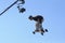 Young boy, the skateboarder, jumping high in the blue sky with the skateboard, tv camera on a background