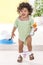 Young boy standing in green knitted jumpsuit , diapper on legs, holding water from a bottle iwitn a white and blue potty